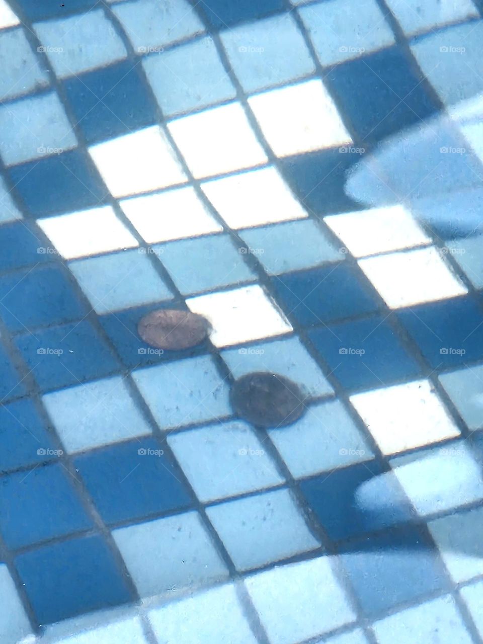 two coins on the blue and white checkerboard pattern tiles underwater in a wishing fountain