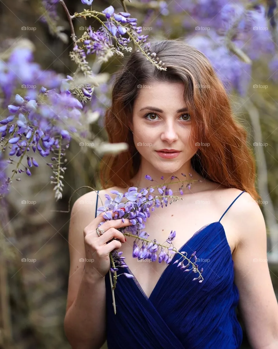 A young girl with long beautiful hair on a background of spring flowers. Natural beauty. Hair health and beauty thanks to hair care cosmetics Herbal Essences.