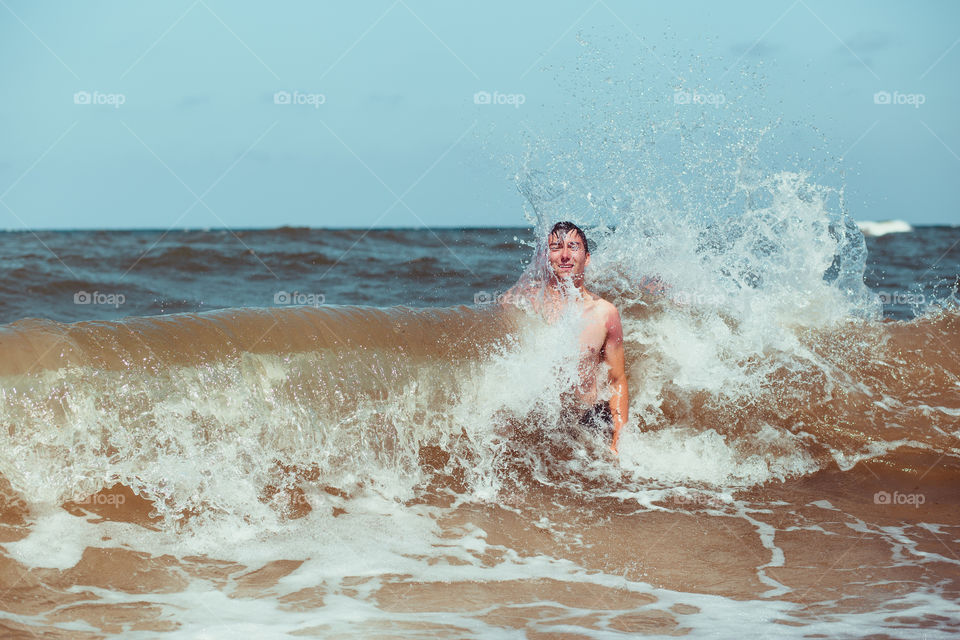 Young man enjoying the high waves in the sea during a summer vacations. Spending a summer holiday by the sea