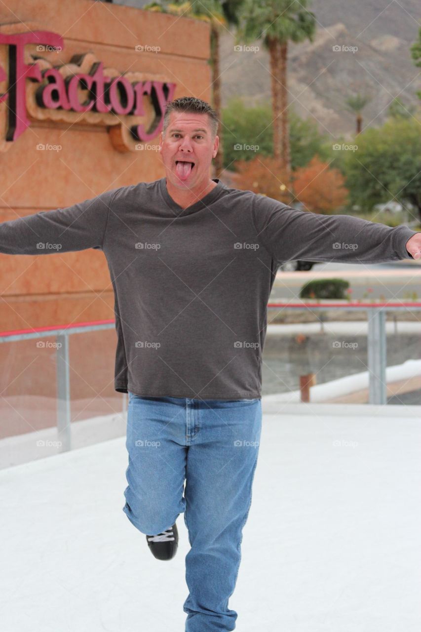 father ice skating towards his kids making a funny face as he stretches out his arms to hug them