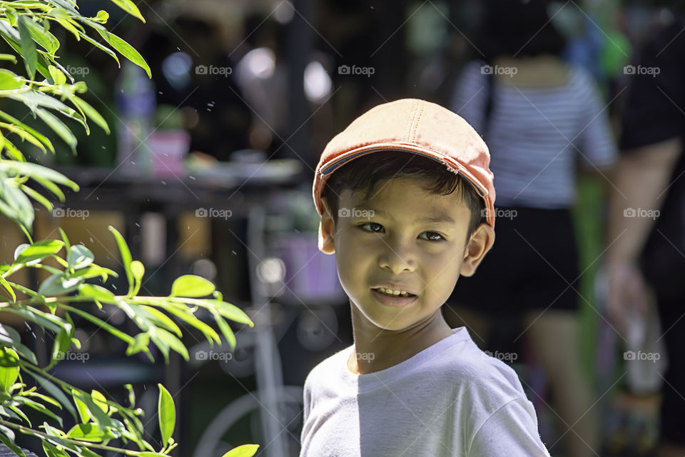 Portrait of Asian boy wearing a red cap and white  shirt is smile and Play water mist.