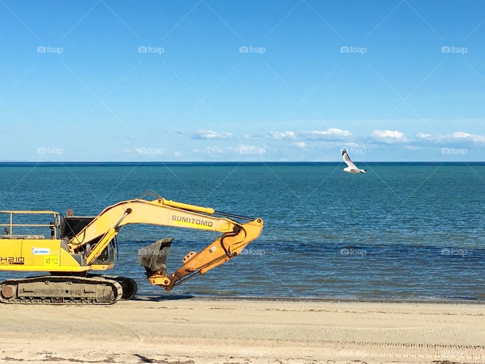 Sumitomo yellow excavator heavy machinery traveling along south Australian beach 