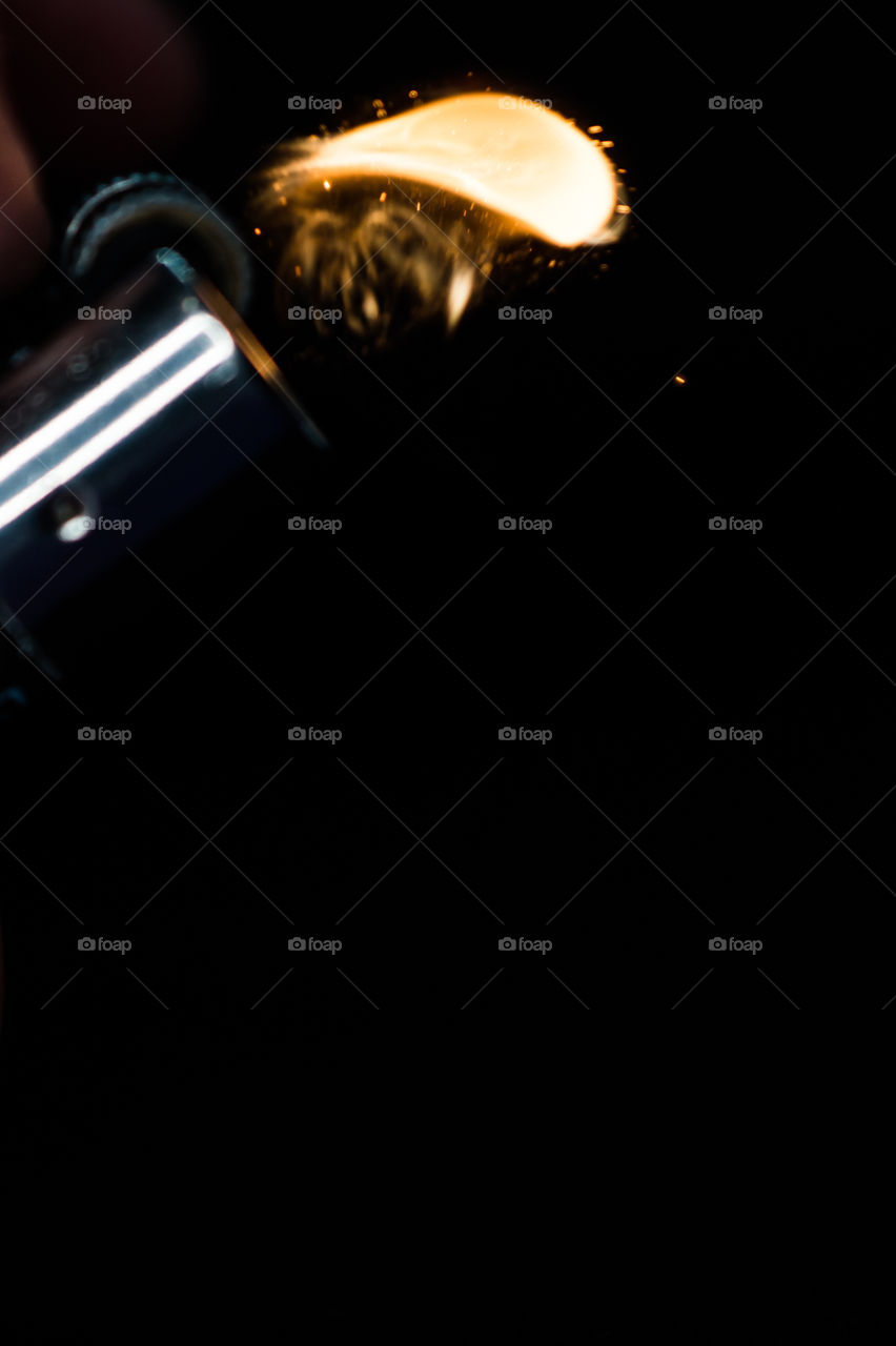 A person has lighters in his hands and he lights it through a flint wheel, the lighter ignites, sparks and fire appear, close-up on a black background.