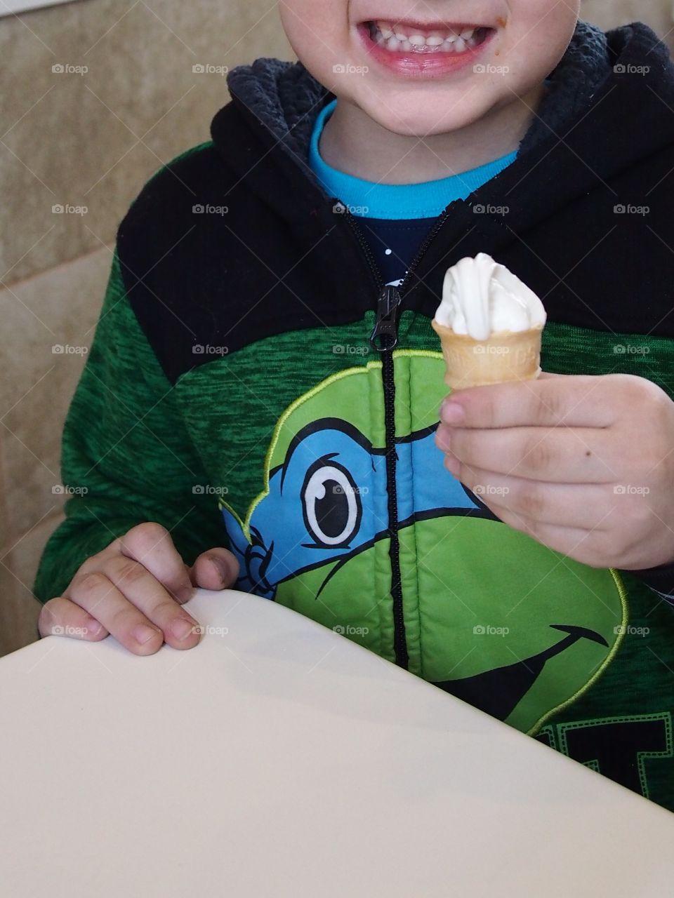 A little boy really enjoys his small vanilla cone that really hits the spot. 