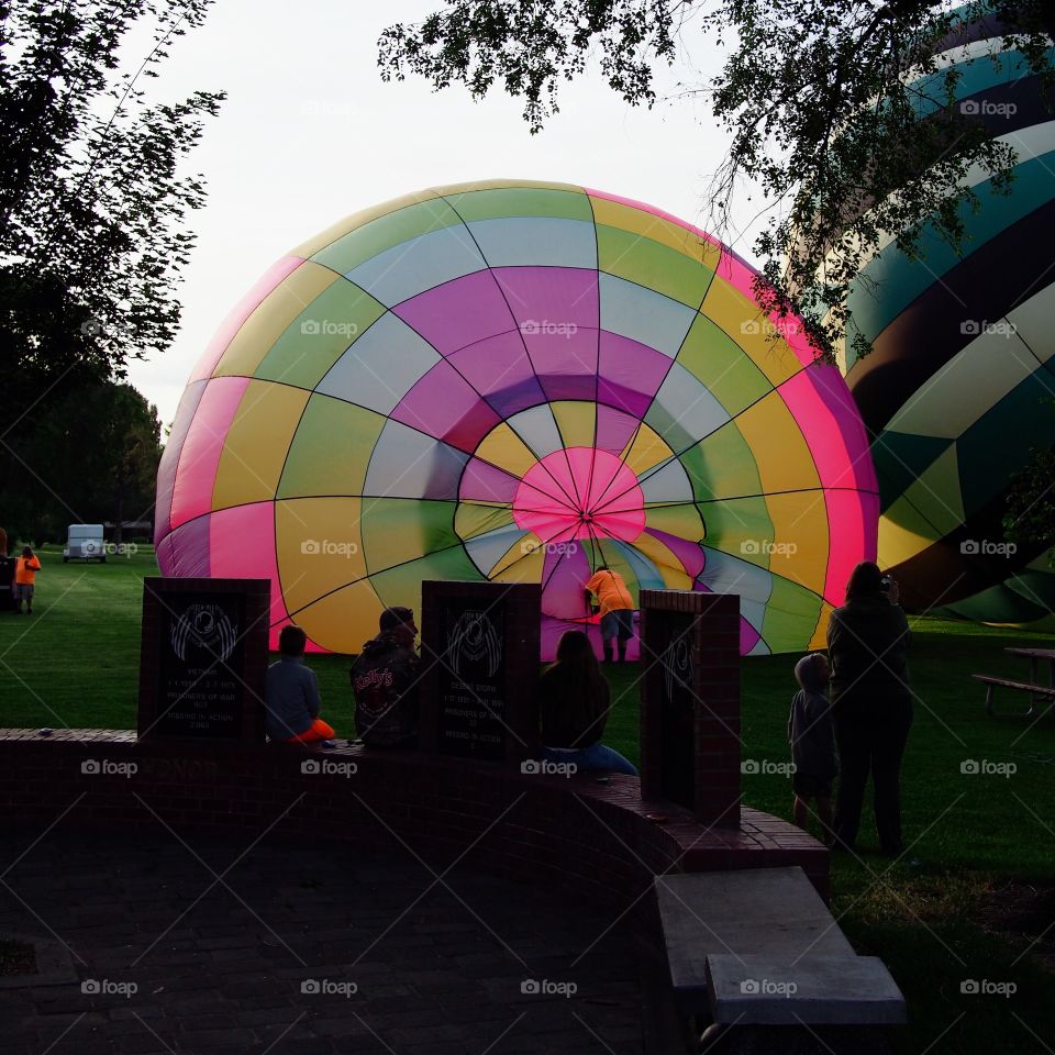 Two bright and colorful hot air balloons on the grass of Ochoco Park filling with helium for a morning flight over Prineville in Central Oregon while a crowd watches from the towns memorial on a beautiful summer morning as the sun rises.