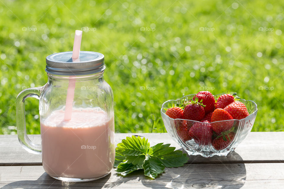 Summer, enjoying fresh strawberries and strawberry smoothie in a glass jar with lid and straw 