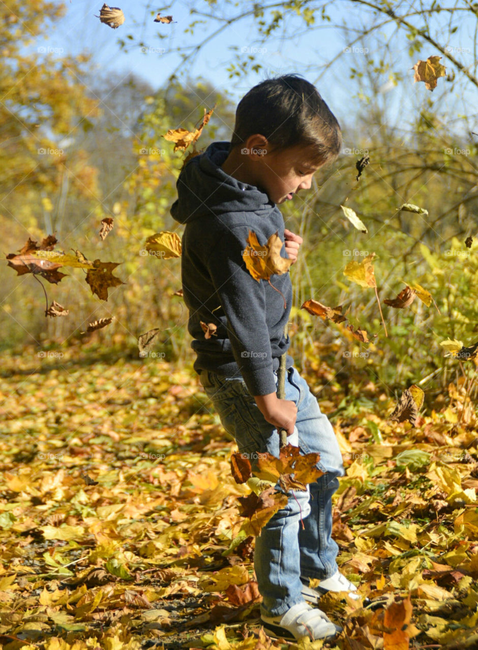 pojke leker med löv i höstsolen