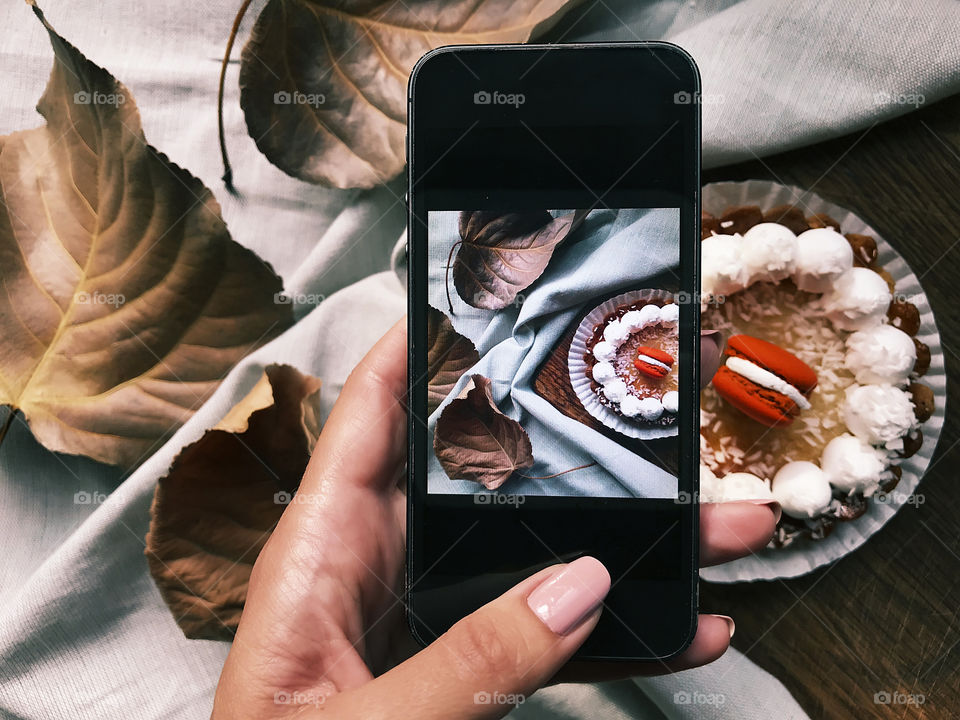 Female hand taking a photo of a cake with a red macaroon