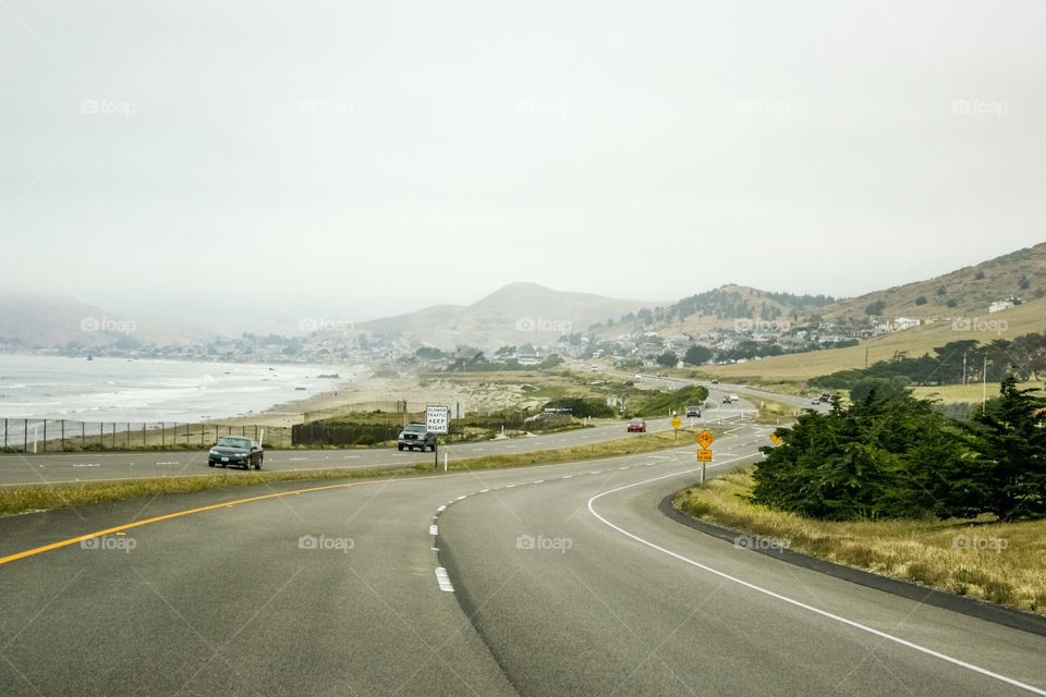 Southern California coast road, Highway 1, curves to the right then left. Cars are seen driving on a misty day in May.