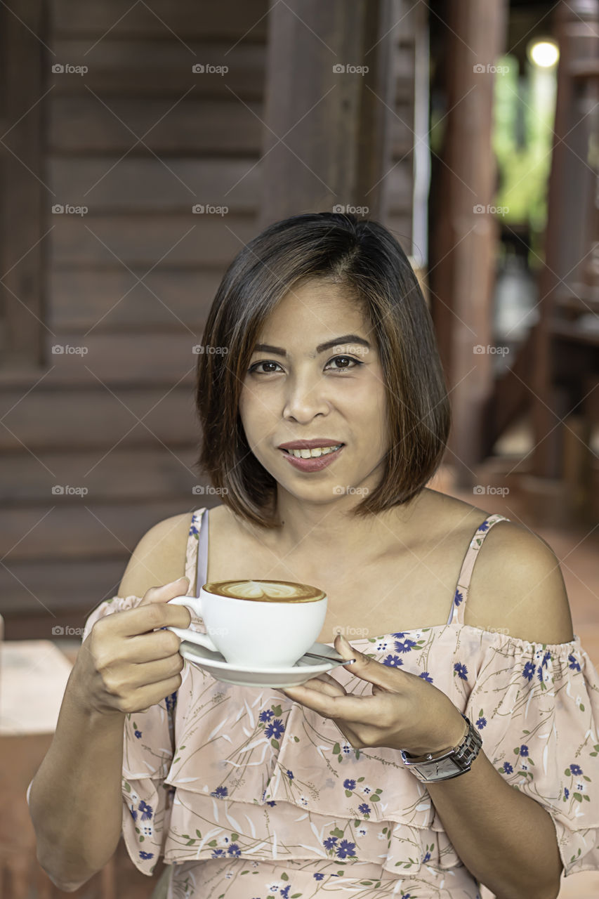 Hand Asian woman holding Hot coffee Espresso topped with a heart-shaped milk in white glass.