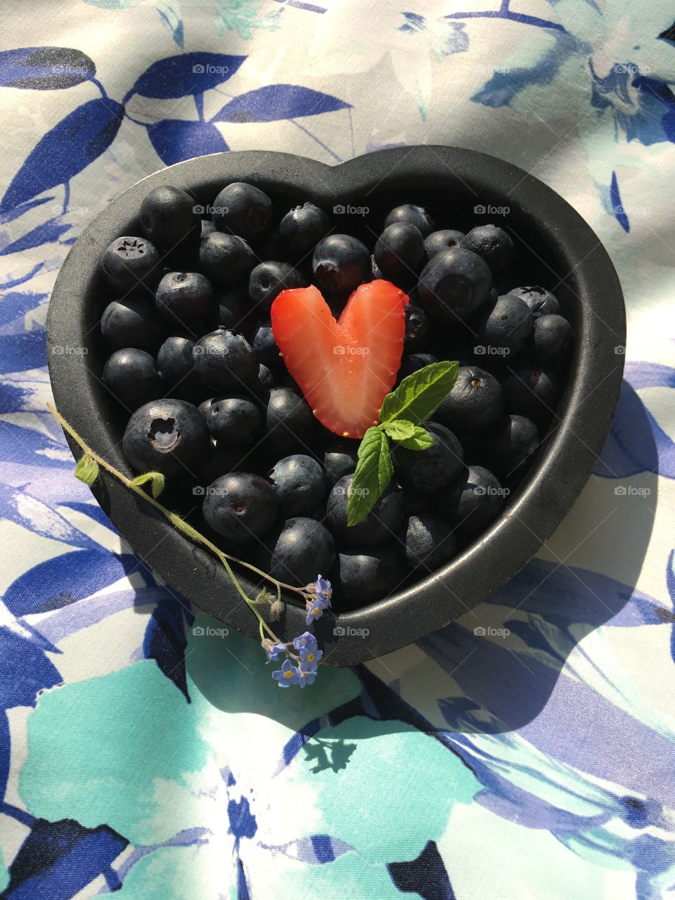 Blueberries in a heart shaped tin with a heart shaped strawberry, sprig of mint and a stem of forget me not flowers 