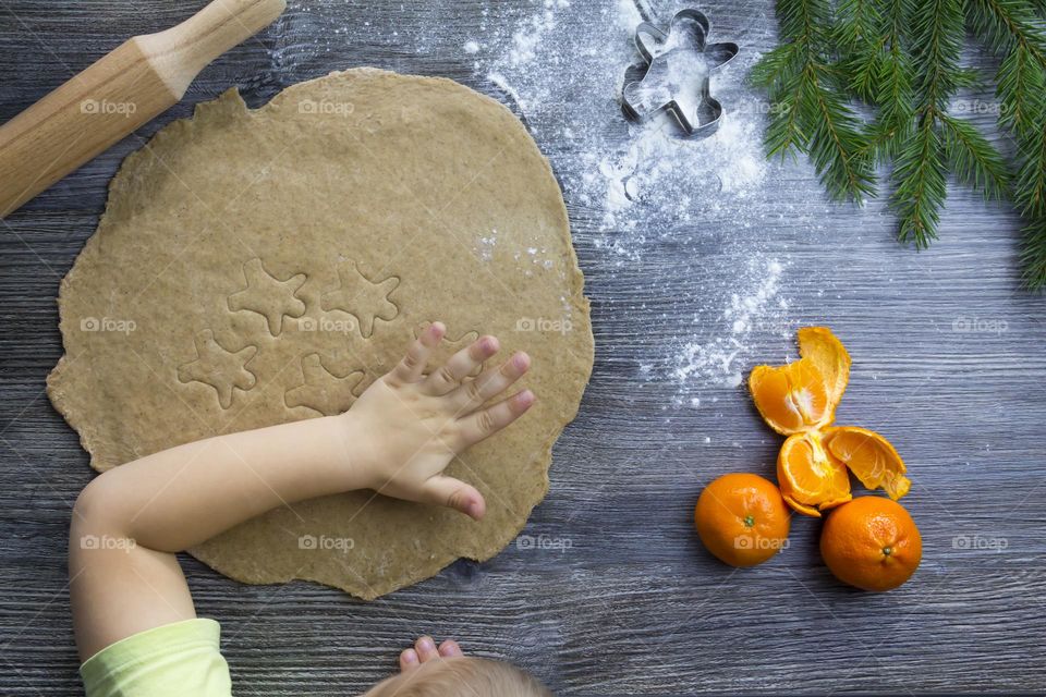 A small child helps to prepare festive, gingerbread cookies on a wooden table on Christmas Eve.