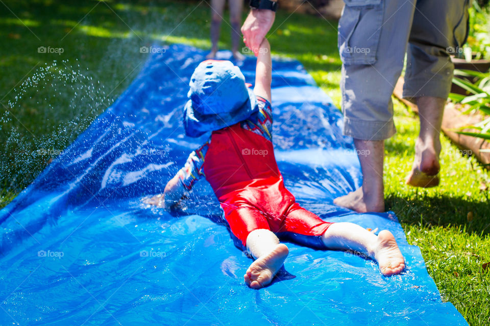 We're in lockdown but that didn't stop us having fun - image of dad and son playing on a slip 'n slide with water drops in the garden