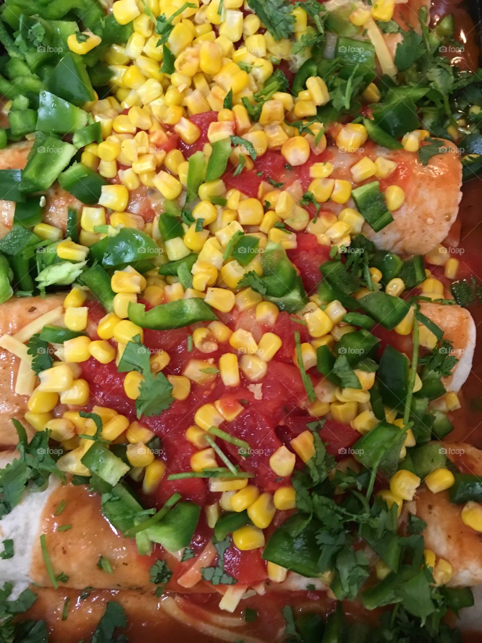 Beef enchiladas in baking pan topped with cilantro (coriander) sweet corn, tomatoes and enchilada sauce