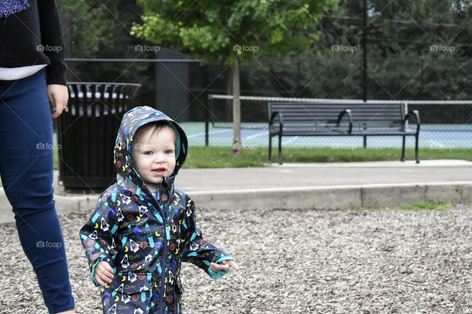 Cute toddler boy in raincoat playing at playground 