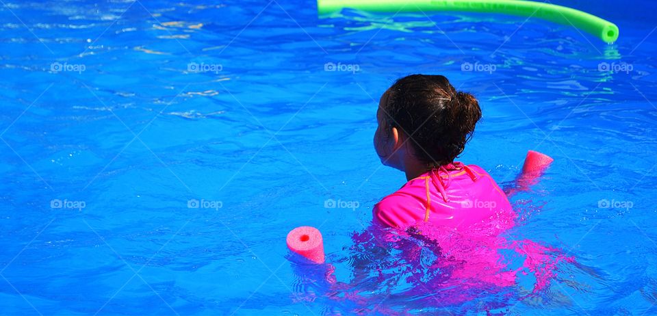 Little girl swimming. Little girl in  pink having fun in swimming pool with pool toys