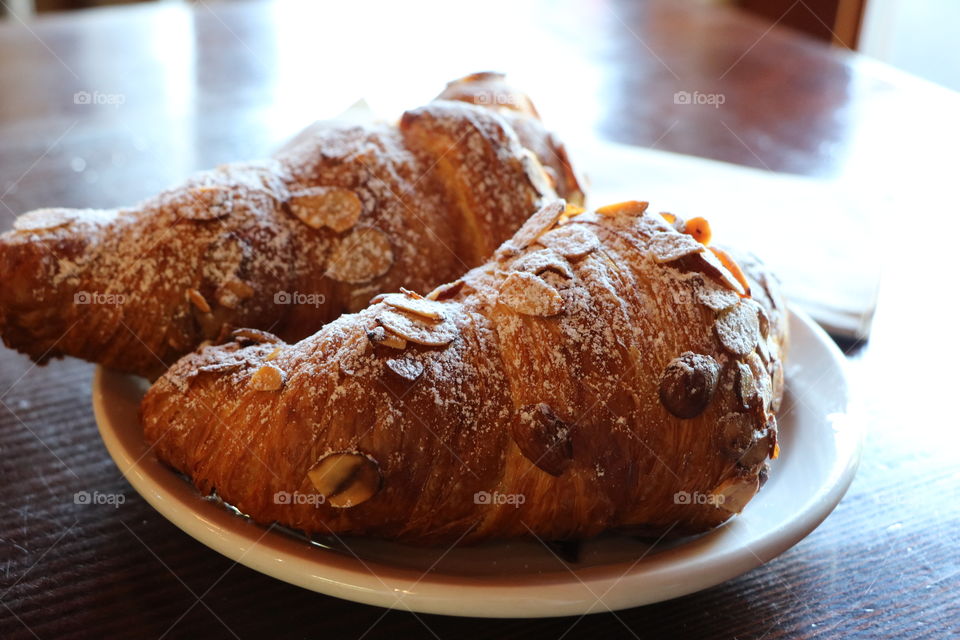 Freshly baked almond croissants for breakfast in a plate on a wooden table- let’s eat !