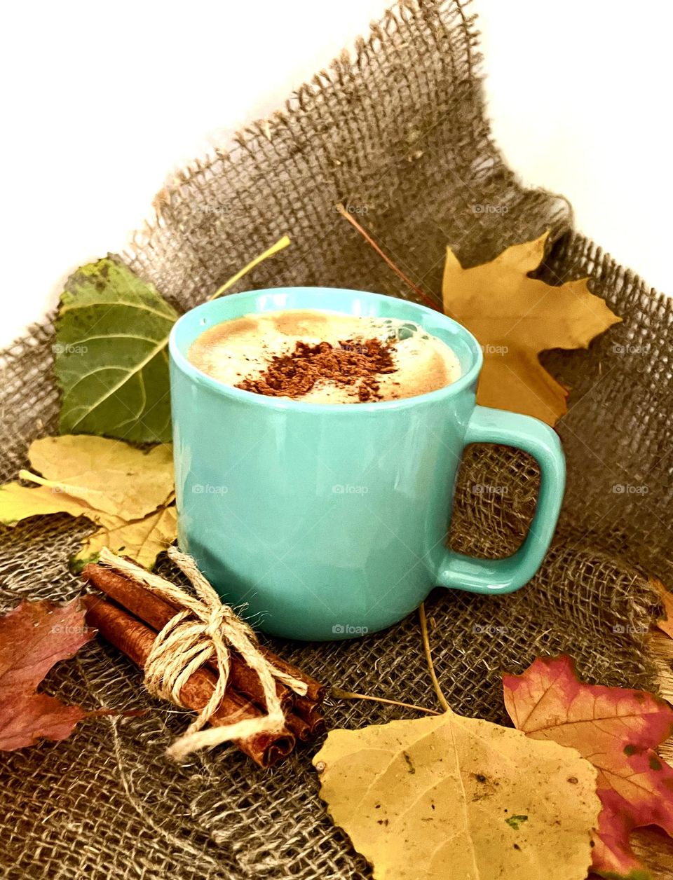 Blue cup of coffee with cinnamon on burlap fabric and yellow leaves background