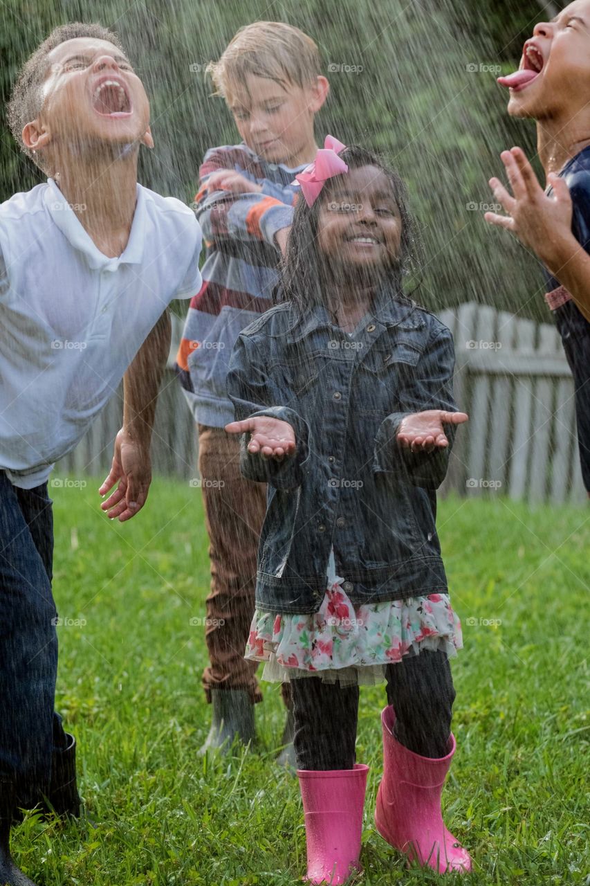 A cute little girl closes her eyes and enjoys the feel of the cool refreshing water from the sprinkler as the others are more in active glee. All in dress clothes, and all could care less:). FUN!
