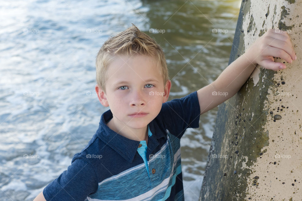 Boy posing near a pier at the beach serious face