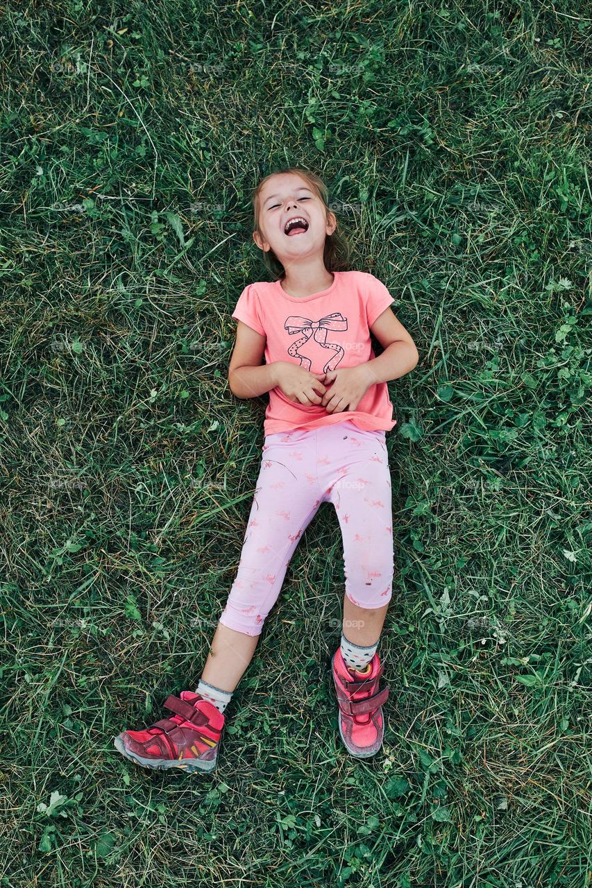 Little girl laying playing on grass enjoying summer day. Happy child playing in the field during weekend trip