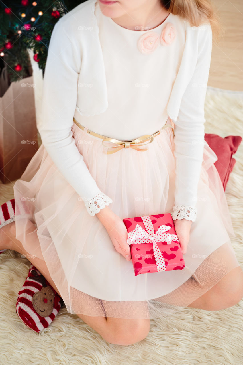 Top shot of girl wearing pink dress holding Christmas gift and sitting on a carpet